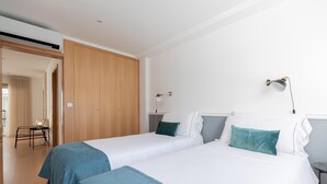 Habitación de hotel con dos camas, un armario de madera, un escritorio con lámpara y vistas al pasillo.