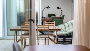 Una habitación con una puerta de cristal que da a un balcón, una mesa de madera con sillas, un sofá verde y dos lámparas fijadas a la pared.