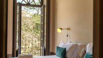 Una habitación de hotel con cama, ventana con vistas a árboles y lámpara fijada a la pared.