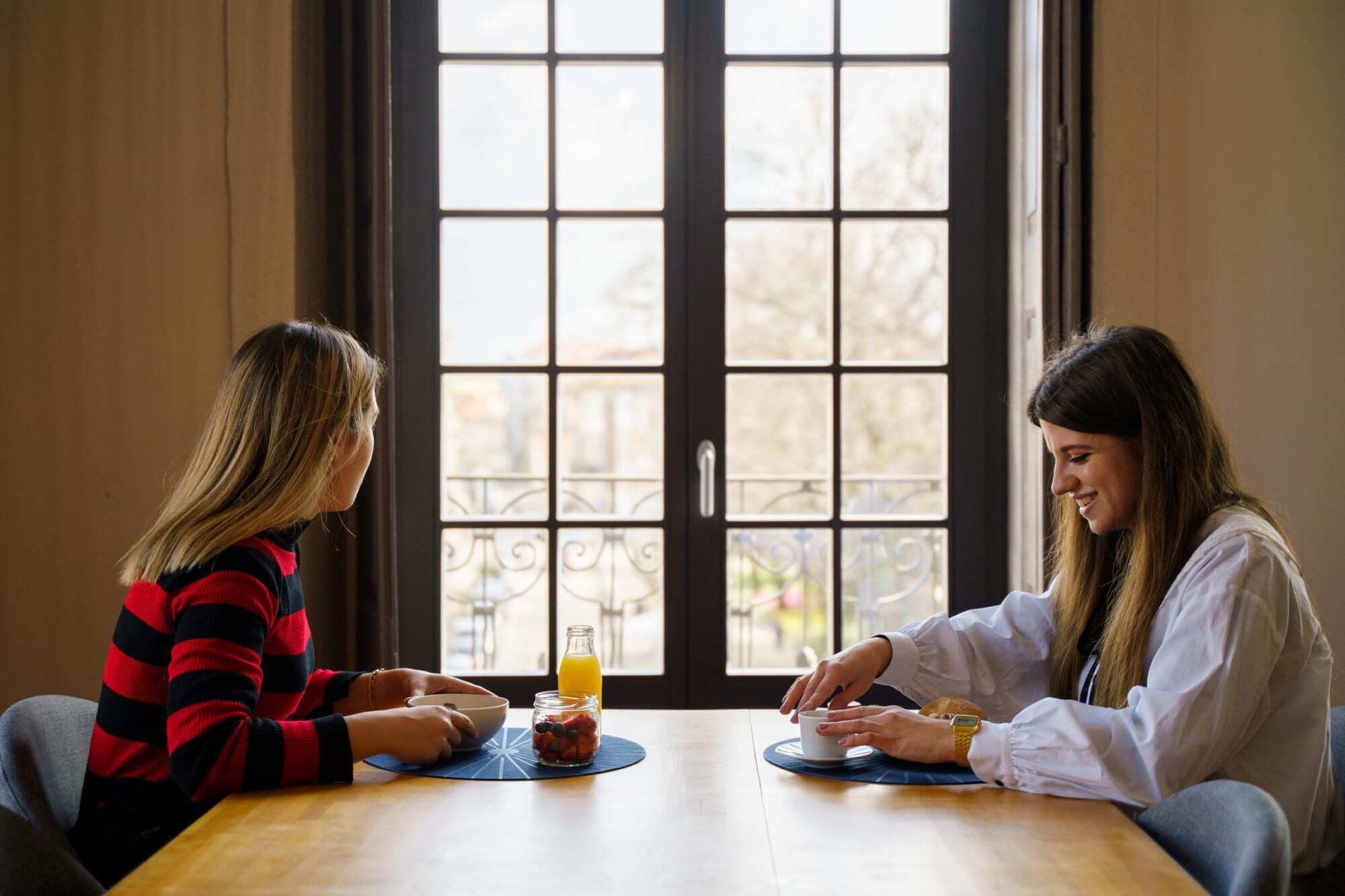 Dos personas sentadas en una mesa de madera con un tazón y un vaso de jugo de naranja.