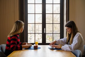 Two people sitting at a wooden table with a bowl and a glass of orange juice. - Feel Porto Antique Poveiros Flat II (Porto)
