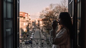 A person standing by a window with a view of a street and buildings. - Feel Porto Antique Poveiros Flat II (Porto)