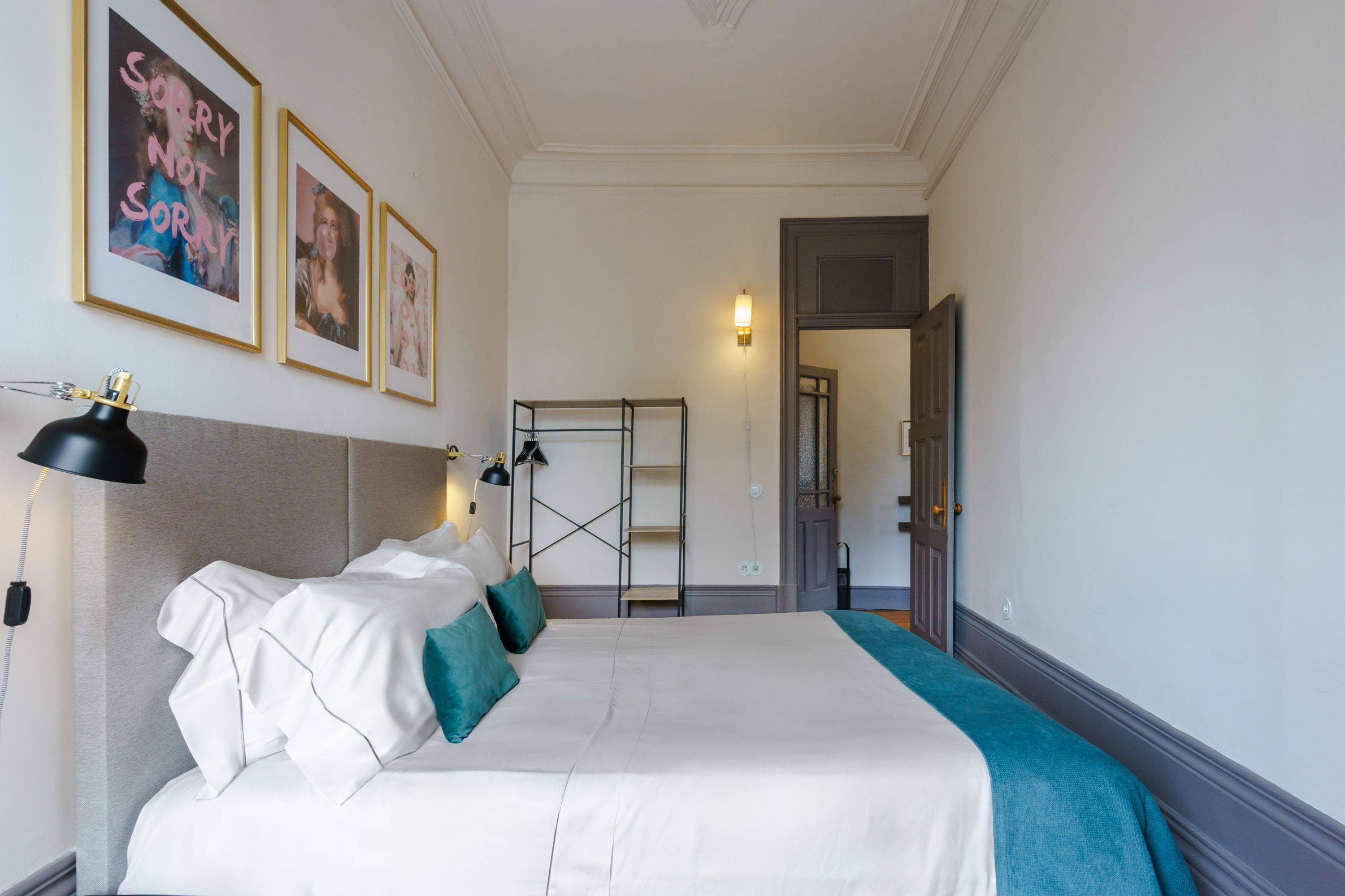 A hotel room with a bed, a bedside table, a lamp, and framed pictures on the wall.