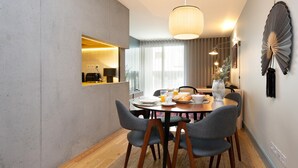 Uma área de refeições moderna com uma mesa redonda, cadeiras estofadas cinzentas e uma luminária pendente.