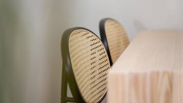 A close-up of a chair with a woven seat and backrest, positioned next to a table with a light-colored tablecloth.