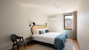 Ein Schlafzimmer mit einem Bett, einem Sessel, einem Nachttisch, einer Lampe und einem Fenster mit Vorhängen.