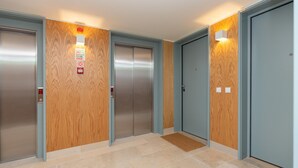 Ein Aufzugsbereich mit vier Aufzügen, Holzvertäfelung an den Wänden und einem gefliesten Boden.