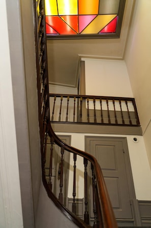 Stunning staircase with a glass door featuring a vibrant stained glass design, leading to an upper landing with a wooden railing.