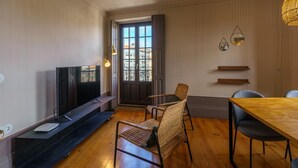 Una sala de estar moderna con un televisor de pantalla plana, una mesa de comedor de madera, sillas de mimbre y un ventanal con vistas a edificios.
