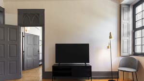 Una sala de estar moderna con un televisor de pantalla plana sobre un soporte negro, un tapete estampado, una lámpara de pie alta y un sillón gris.