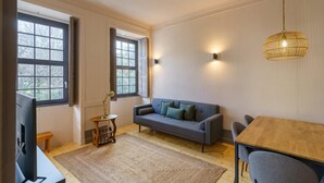 Una sala de estar moderna con un sofá gris, una mesa de comedor de madera y un ventanal con cortinas.