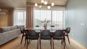 A modern dining area with a wooden table, six chairs, a sofa, and a large window with sheer curtains. - Feel Corporate Housing Campanh 05 (Porto)