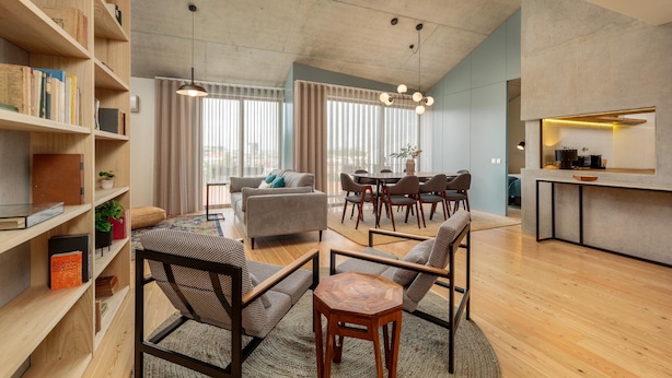A modern living room with a sofa, chairs, a coffee table, a bookshelf, and a dining area with a table and chairs. - Feel Corporate Housing Campanh 05 (Porto)