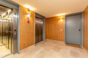 Un espace d’ascenseur avec un lambris en bois, un détecteur d’incendie et une porte dotée d’un paillasson.