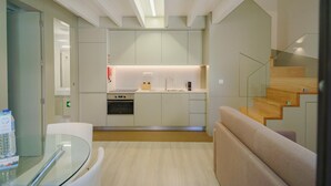 A modern kitchen with a built-in oven and sink, a glass table with a water bottle, and a staircase leading to another level. - Feel Porto Matosinhos Ocean Flat V (Matosinhos)