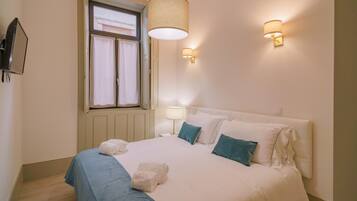 A bedroom with a bed, two wall-mounted lamps, a window with curtains, and a television on the wall.