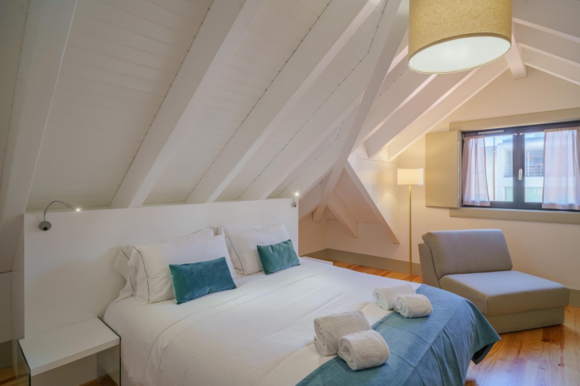 A bedroom with a large bed, a chair, a lamp, and a window.