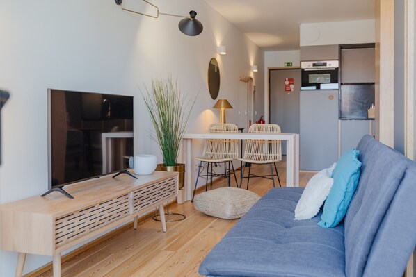 A modern living room with a flat-screen TV, a sofa, a coffee table, and a dining area with chairs and a table.
