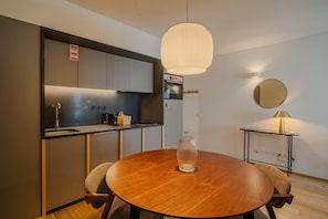 Une cuisine moderne dotée d’appareils électroménagers en acier inoxydable, d’une table de salle à manger ronde en bois et d’un luminaire suspendu.