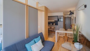 A modern living room with a sofa, a dining table with chairs, and a kitchen area in the background. - Feel Corporate Housing Campanh 08 (Porto)