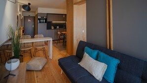 A modern living room with a dark blue sofa, wooden flooring, and a dining area with white chairs and a table. - Feel Corporate Housing Campanh 08 (Porto)