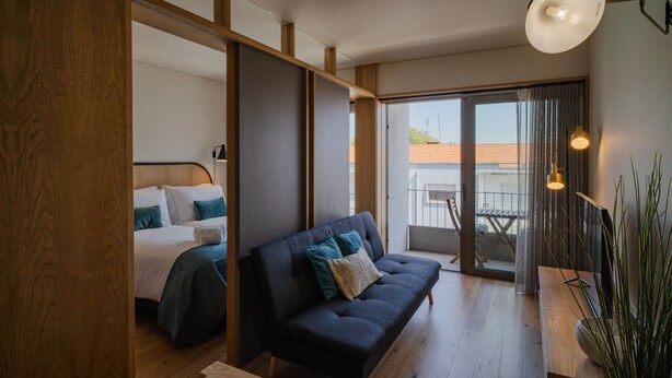 A modern bedroom with a bed, a dark sofa, and a balcony with a view. - Feel Corporate Housing Campanh 08 (Porto)