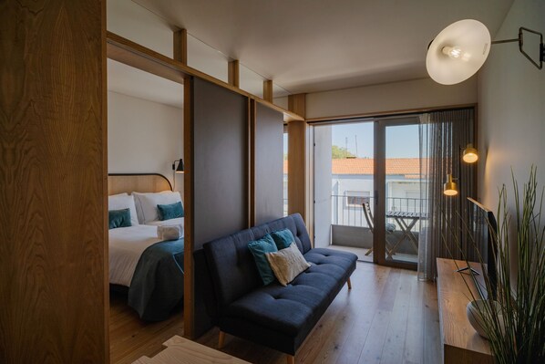 Ein modernes Schlafzimmer mit einem Bett, einer dunklen Couch und einem Balkon mit Aussicht.