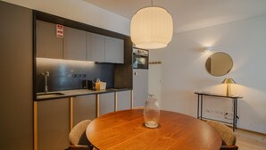 A modern kitchen with a round wooden table, a hanging light fixture, and a small side table with a lamp. - Feel Corporate Housing Campanh 08 (Porto)