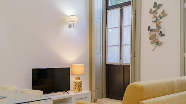 Una sala de estar moderna con un televisor de pantalla plana, una lámpara, un sofá y un elemento decorativo en la pared.