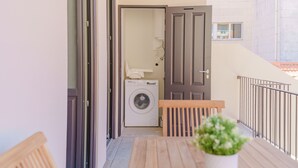 A balcony with a wooden table, a potted plant, and a washing machine in the background. - Feel Porto Matosinhos Ocean Flat III (Matosinhos)