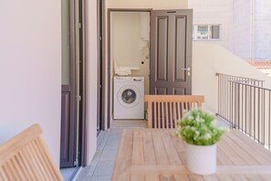 A balcony with a wooden table, a potted plant, and a washing machine in the background. - Feel Porto Matosinhos Ocean Flat III (Matosinhos)