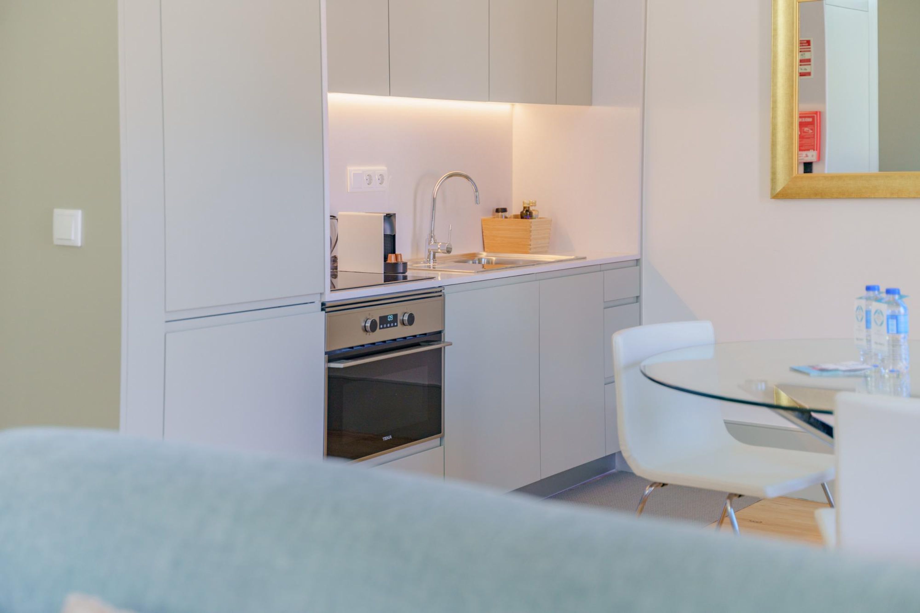 A compact kitchen with a built-in oven, a sink, and a small dining area with a glass table and white chairs.