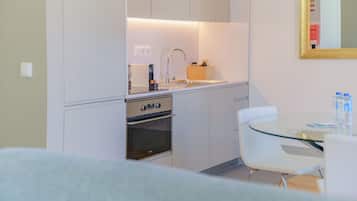 A compact kitchen with a built-in oven, a sink, and a small dining area with a glass table and white chairs.