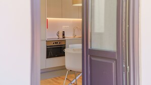 A modern kitchen with stainless steel appliances, a white chair, and a wooden floor. - Feel Porto Matosinhos Ocean Flat III (Matosinhos)