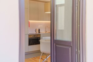 A modern kitchen with stainless steel appliances, a white chair, and a wooden floor. - Feel Porto Matosinhos Ocean Flat III (Matosinhos)