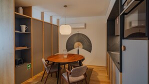 A compact dining area with a round wooden table, four chairs, a hanging fan, and built-in shelving with kitchenware. - Feel Corporate Housing Campanh 10 (Porto)