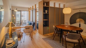 A modern living room with a wooden dining table, wicker chairs, a sofa, and a large window. - Feel Corporate Housing Campanh 10 (Porto)