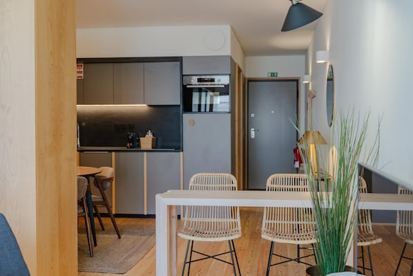 A compact kitchen with modern appliances, a dining area with white chairs, and a small table. - Feel Corporate Housing Campanh 07 (Porto)