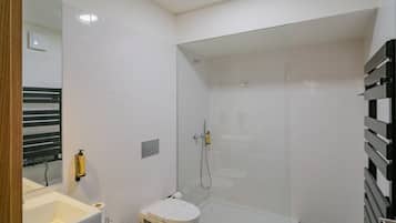 Uma casa de banho moderna com cabine de duche em vidro, sanita branca e lavatório com espelho.