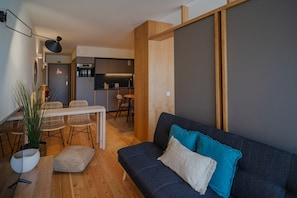 A modern living room with a dark blue sofa, wooden flooring, and a dining area with white chairs and a table. - Feel Corporate Housing Campanh 07 (Porto)