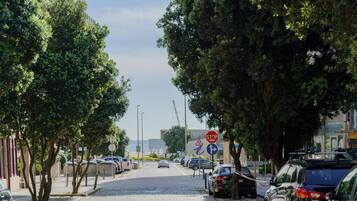 Calle adoquinada bordeada de coches aparcados y árboles. Se observan una señal de stop y una señal de dirección.