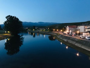Un río tranquilo que refleja luces, rodeado de edificios y un árbol.