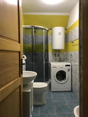 Baño pequeño con inodoro, lavadora y cabina de ducha.