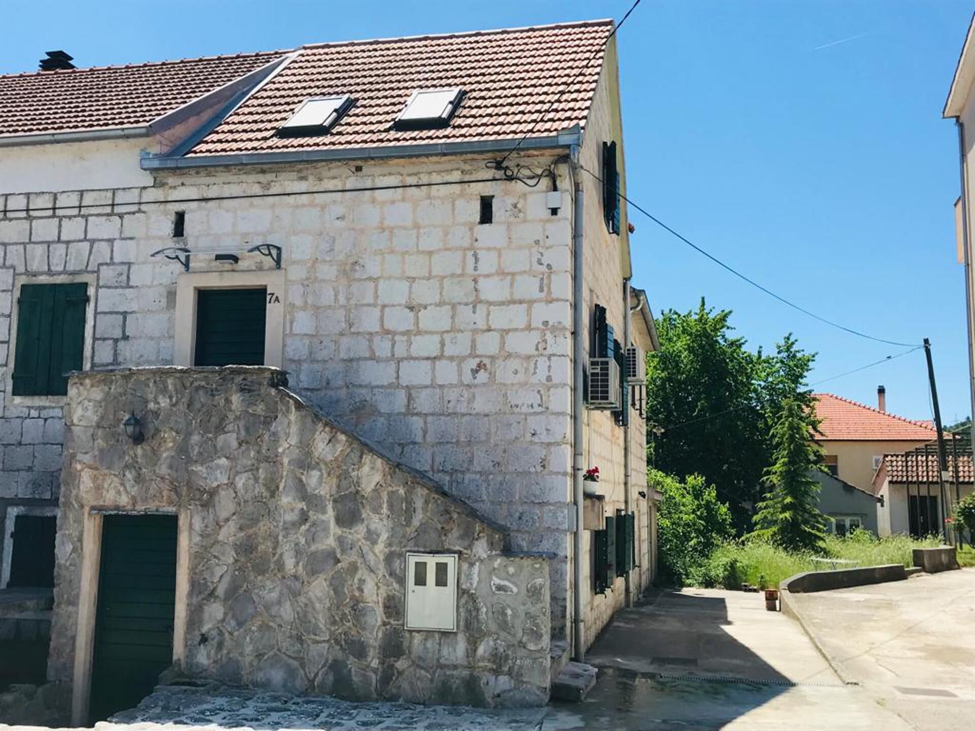 A stone building with a tiled roof, a small staircase, and a narrow pathway leading to another building.