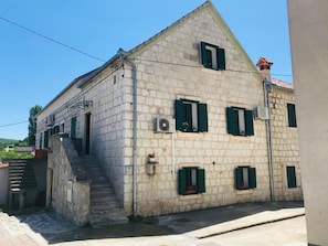 A stone building with a staircase leading to the entrance, multiple windows with shutters, and a visible air conditioning unit. - Stone House Saint Michael (Trilj)