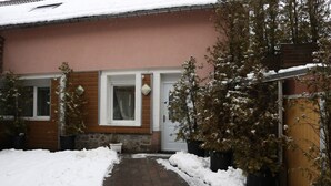 Una casa con un vialetto in mattoni che conduce a una porta in legno, immersa in un terreno coperto di neve e circondata da vasi con piante.