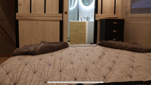 Una camera da letto con un letto, un armadio in legno e un bagno visibile attraverso una porta aperta.