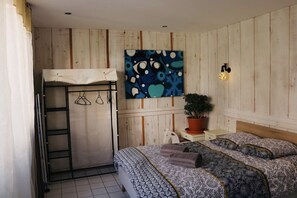 Um quarto com uma cama de solteiro, um guarda-roupa, uma pintura, um vaso de planta e uma pequena escrivaninha.