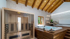 Uma sala de sauna com divisória de vidro, um banco de madeira e uma banheira de hidromassagem com degraus.