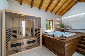Een sauna met een glazen wand, een houten bank en een whirlpool met treden.